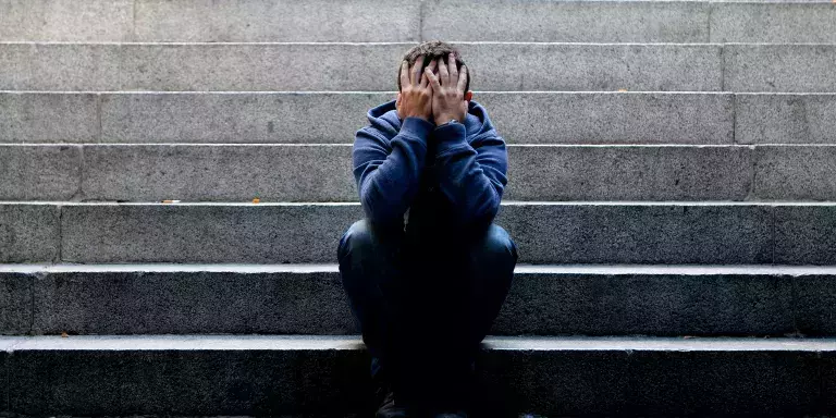 Man sitzt auf einer Treppe und hält sich die Hände vor das Gesicht